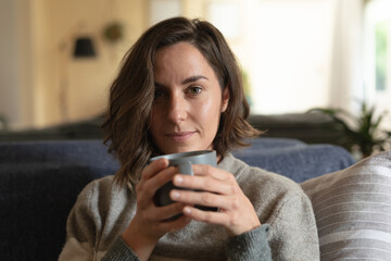 Portrait of smiling caucasian woman in living room sitting on sofa and drinking coffee