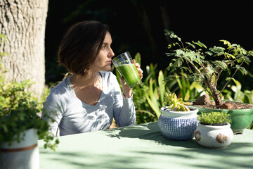 Caucasian woman in garden, sitting at table drinking health drink