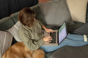 Caucasian woman in living room, sitting on sofa with her pet dog, using laptop