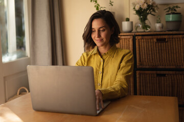 Caucasian woman in living room sitting at table, working using laptop
