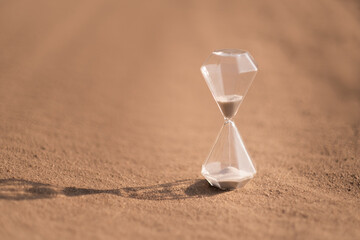 An hourglass on hot sand in desert in hot summer sun.