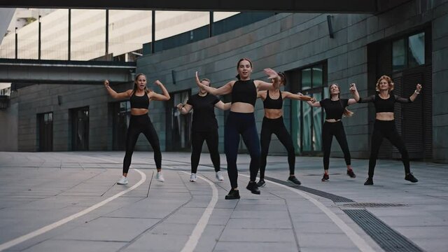 Slow motion group of girls under the guidance of a trainer perform a set of aerobics exercises and dance zumba. Outdoor morning warm-up