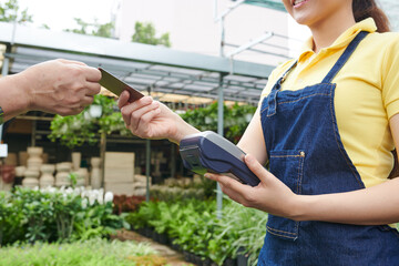 Positive young plant nursery worker taking credit card and accepting payment