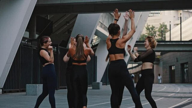 Group of girls in black jerseys give each other a high five outdoors. Group high five. Six beautiful young athletes rejoice and celebrate the victory