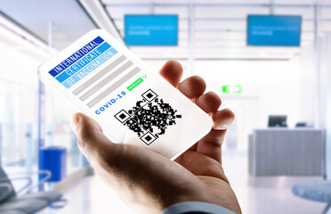 coronavirus, technology and health concept - close up of man's hand holding transparent smartphone with international certificate of covid-19 vaccination on screen over airport lounge background
