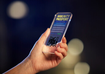coronavirus, technology and health concept - close up of woman's hand holding transparent smartphone with international certificate of covid-19 vaccination on screen over dark night background