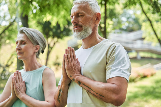 Serene mature married couple enjoying meditation around the trees