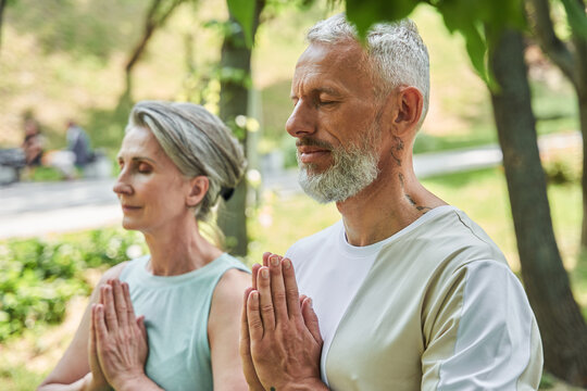 Serene mature married couple enjoying meditation around the trees