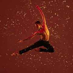 One young male ballet dancer in motion, action under the rain over red background in neon light.