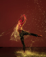 Passion, emotion. One young male ballet dancer in motion, action under the rain over red background in neon light.