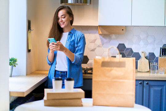 Modern busy cute smiling joyful happy casual millennial woman received cardboard bags and paper cups with takeaway food and drinks. Fast home delivery concept