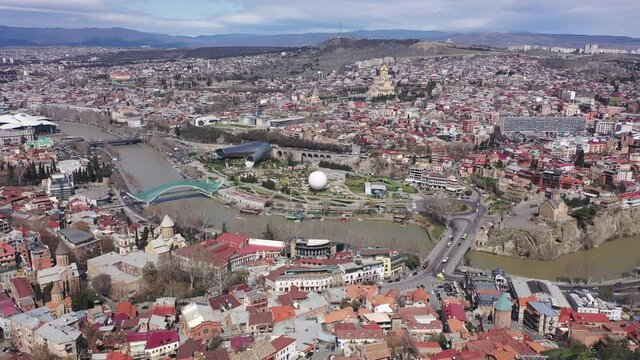 Scenic cityscape of historical area of Tbilisi overlooking Holy Trinity Cathedral with golden dome in background and small Metekhi Church on steep bank of Mtkvari River on sunny spring day, Georgia. 