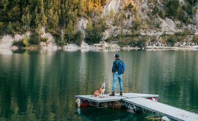 Walking in nature concept image. Male dog owner and his friend beagle dog on the wooden pier on the mountain lake during their together walking in the autumn season time. Human and pet concept image.