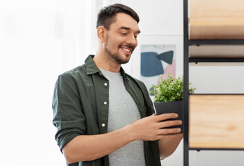 Fototapeta premium home improvement, decoration and people concept - happy smiling man placing flower in pot or houseplant to shelf