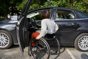 Fototapeta premium Woman in a wheelchair getting on the car at the drivers sit and preparing to the road