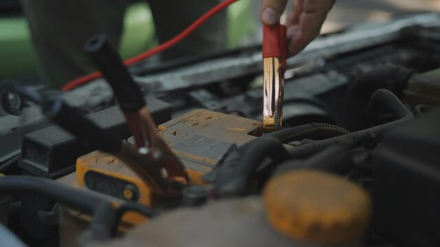 The man connects cables with metal probes to the car's battery to recharge it.