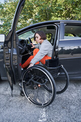 Fototapeta na wymiar Woman in a wheelchair getting on the car at the drivers sit and preparing to the road