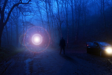 A man next to a car looking at a glowing UFO, floating above a track in a spooky misty forest,...