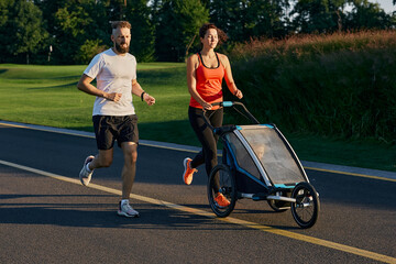 Active family running. Young family with their kid in a jogging stroller during jogging in a public...