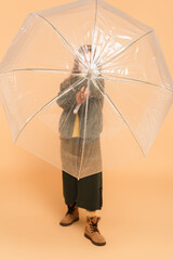 stylish child hiding behind transparent umbrella on beige