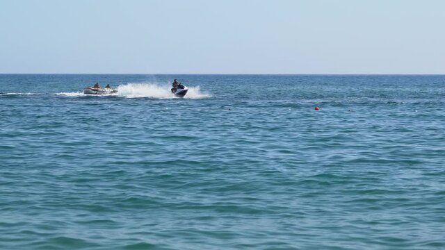 People in a Jet ski and inflatable dinghy enjoying a summer day on the ocean racing around in circles on a calm sea with copyspace