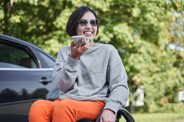 Woman sitting at the wheelchair and recording voice message at her mobile phone