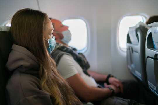 Young Lady With Face Mask Looking Outside Airplane Window