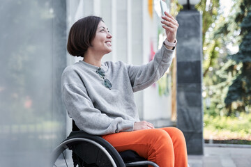 Disabled woman holding smartphone and looking at screen while sitting at the wheelchair