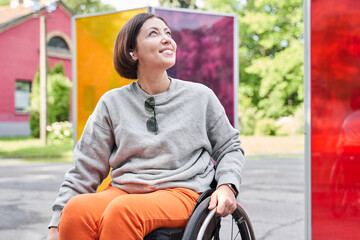 Woman wearing earphones looking away with pleasure smile while sitting at the wheelchair