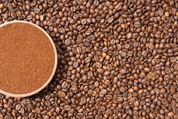 Ground coffee in wooden plate on coffee beans background. Top view. Copy space