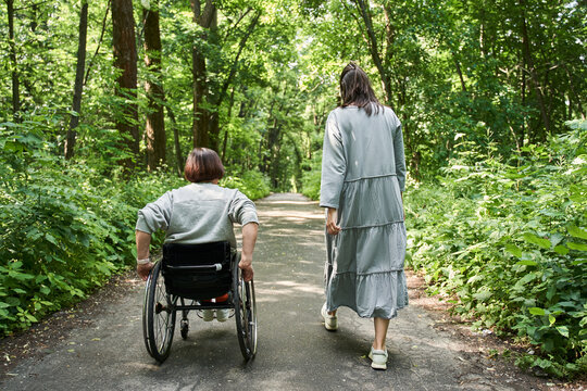 Disabled woman in wheelchair moving herself while walking with her friend through the path