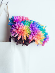 A bouquet of colored chrysanthemums in a white bag on a white background, copyspace. Chrysanthemum is painted in rainbow colors. The bag hangs on a black hook.
