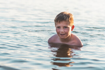 Fototapeta na wymiar Cute young boy enjoy having fun at lake or river beach water on warm sunset evening time outdoors.