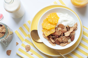Whole grain oats and wheat flakes with orange, almond nuts and yogurt in a white bowl. Healthy morning breakfast concept 