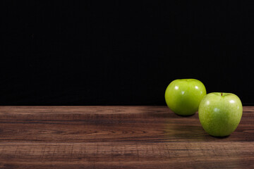 Manzanas rojas y verdes sobre madera rustica oscura y fondo negro.