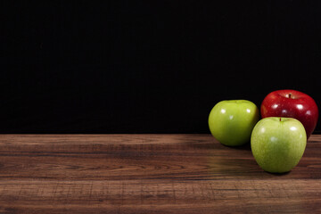 Manzanas rojas y verdes sobre madera rustica oscura y fondo negro.