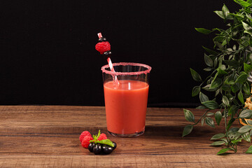 Zumo de frutas junto a manzanas y durazno sobre mesa de madera y fondo negro .
