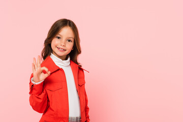stylish girl showing ok gesture while looking at camera isolated on pink