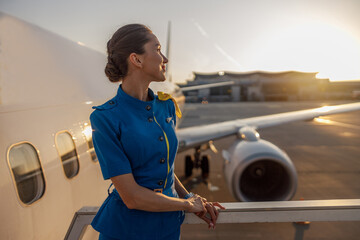 Thoughtful air stewardess in blue uniform looking away, standing outdoors at the sunset. Commercial...