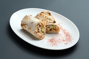 shawarma or pita roll with meat and vegetable on white plate on grey background