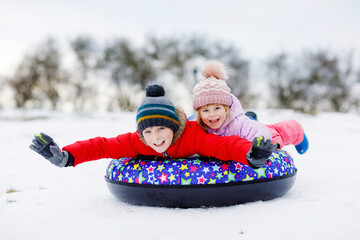 Active toddler girl and school boy sliding together down the hill on snow tube. Happy children,...