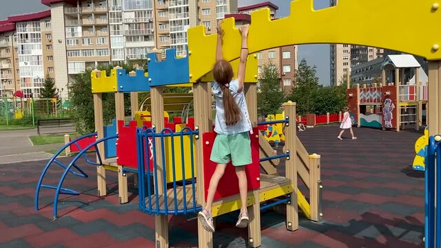Girl with long hair climbs the colorful construction with ladder fences in the playground 