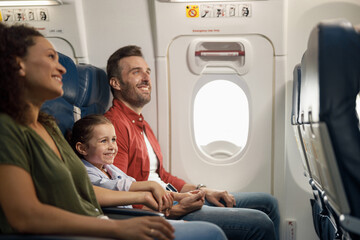 Happy caucasian family, parents with little daughter smiling and holding hands together while sitting on the airplane. Transportation, vacation concept