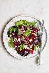 Beetroot salad with feta cheese and walnuts. Vegetable salad in plate on white marble background, top view
