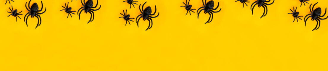Flat lay banner of black horror spiders of different sizes directed in different directions on orange backdrop with copy space. Halloween decoration spooky background concept for holidays