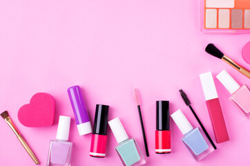 Decorative cosmetics assortment on pink background with copy space. Multicolored nail polish, lipsticks, eyeshadow palette, make-up brushes and sponges. Flat lay