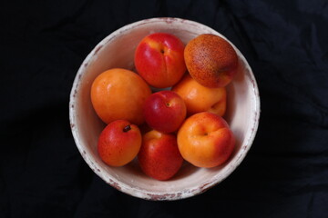 Vintage, white plate full of ripe apricots on a black blurred background 