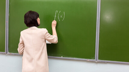 A female teacher writes mathematical formula on a blackboard.