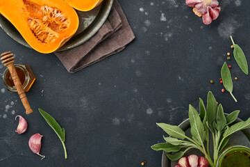 Halves of raw organic butternut squash with sage leaf, multicolored pepper garlic, honey, salt and pepper on black slate, stone or concrete background. Food background. Top view with copy space.