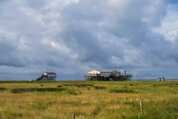 Fototapeta na wymiar Pfahlbauten am Strand von Böhl an der Nordseeküste vor dramatischem Sommerhimmel